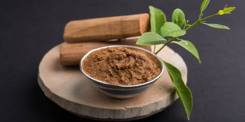 Sandalwood paste in silver bowl with sticks and leaves on a circular stone base for creating paste.