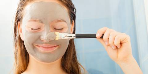 a teenage girl applying a gray mud facial mask