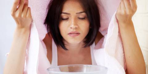 A woman relaxing during a facial steam treatment over a bowl with towel over her head.