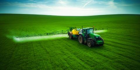 a tractor driving through a field of crops spraying