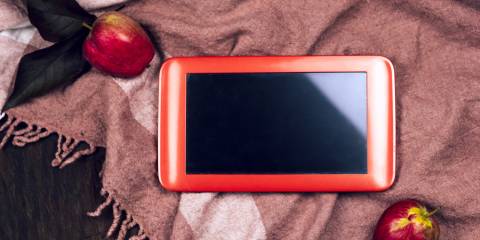 An IPad on a scarf with apples surrounding it.