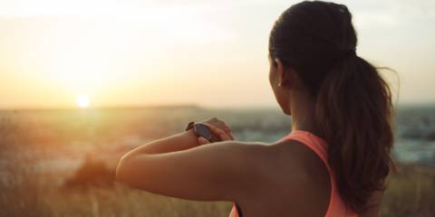 Woman checking workout goals on smart watch looking towards the sunset.