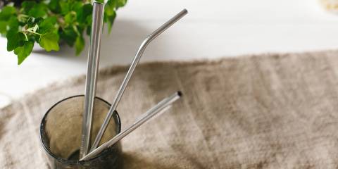 Eco natural metallic straws in green glass on rustic background with greenery.