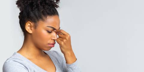 a young woman holding the bridge of her nose due to sinus pain