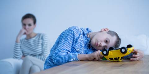An autistic boy playing with a truck while his mother watches