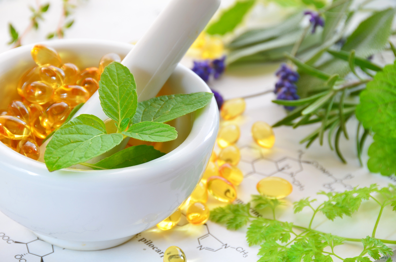 Soft gel supplements in a mortar surrounded by herbs with chemical structure drawings