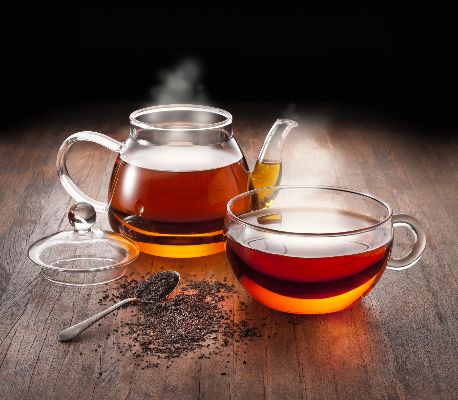 Steaming glass teapot and teacup filled with tea. 