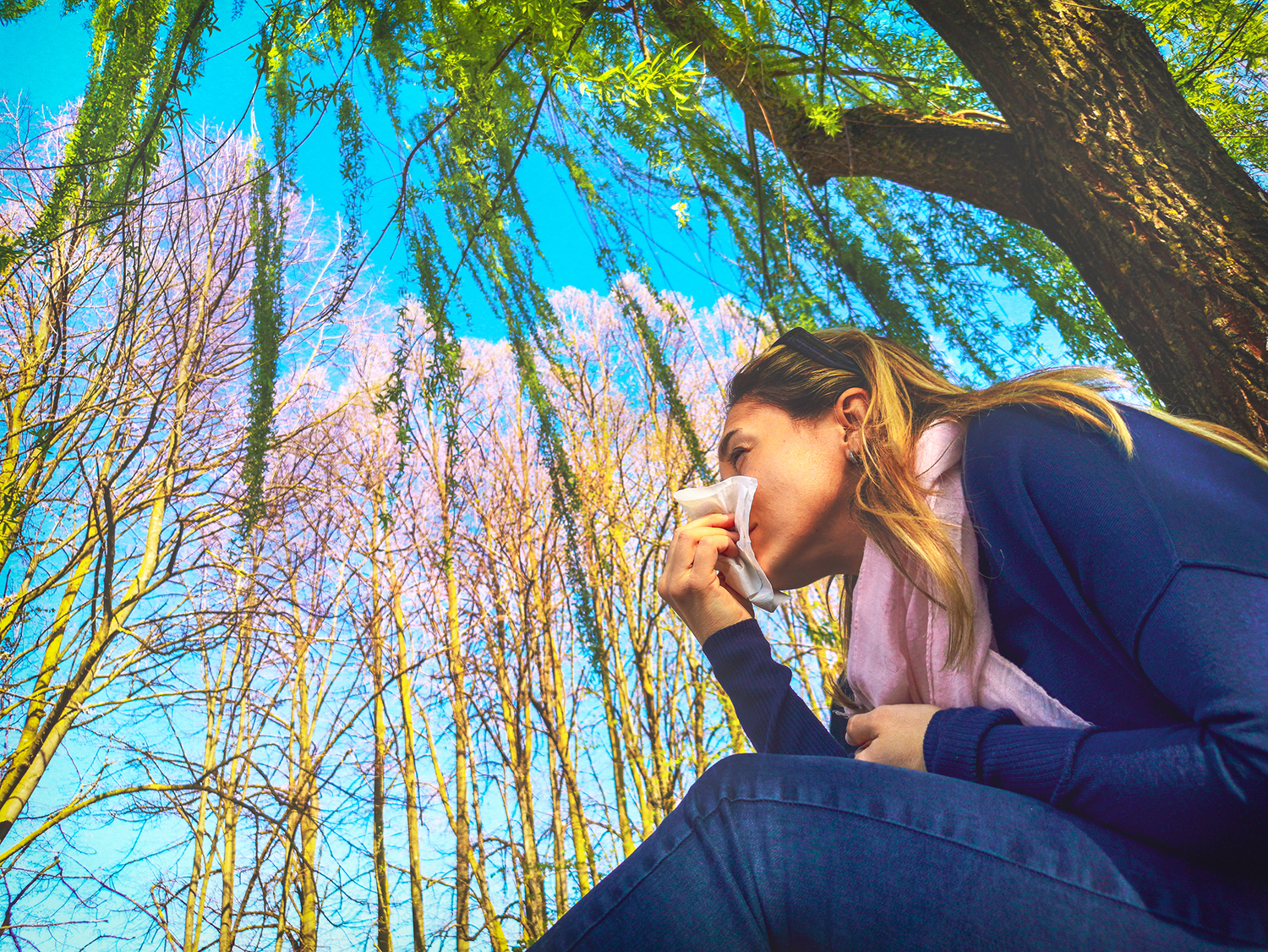 Allergies A woman under a willow tree wiping her nose with a tissue.